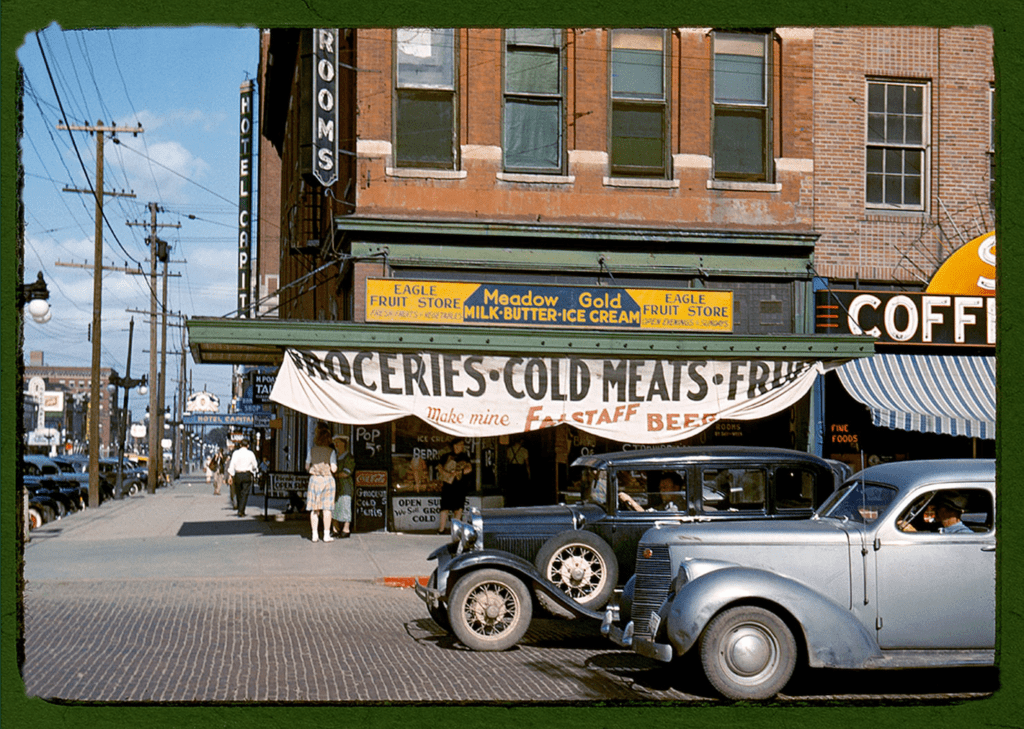 Great Depression era street with cars in front of a general store. Color image.