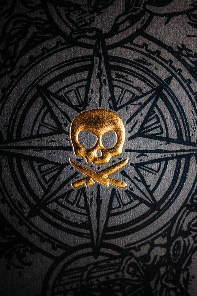 gold-inlayed pirate scull and crossed swords in the center of a black ink compass sketch