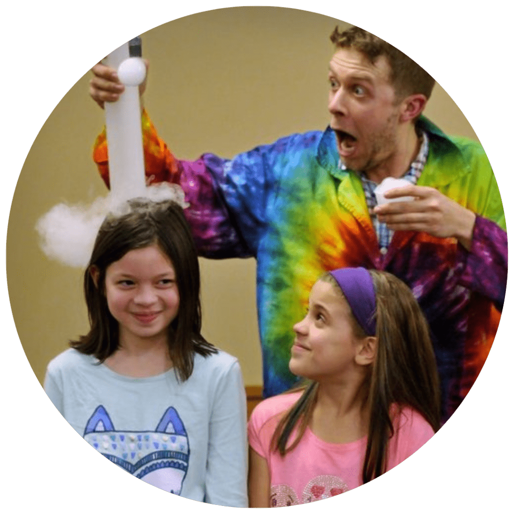 A magician makes a funny face as he performs a trick with two little girls as assistants.