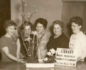 Friends of the Library: Four women with floral display and sign, 1966. Sepia.