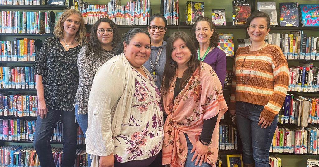 Seven South Branch library staff stand smiling in front of bookshelves.