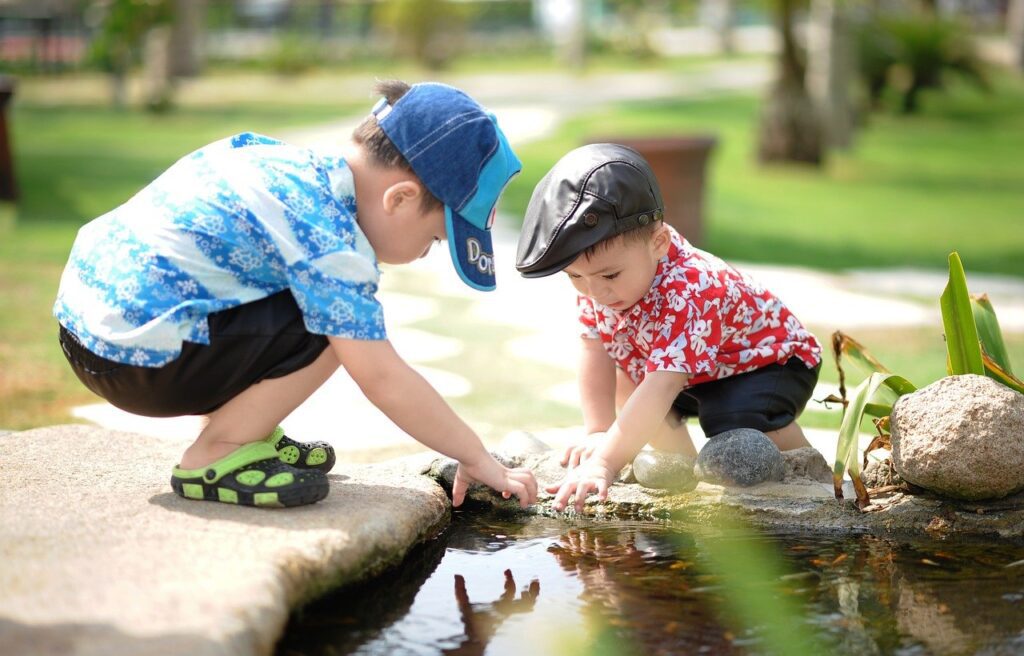 two little boys reaching into a pond in a park
