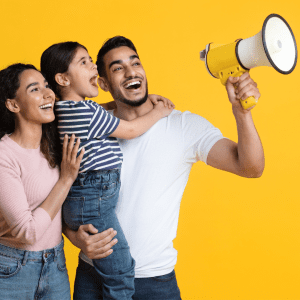 Two smiling parents hold their daughter up to yell into a megaphone.