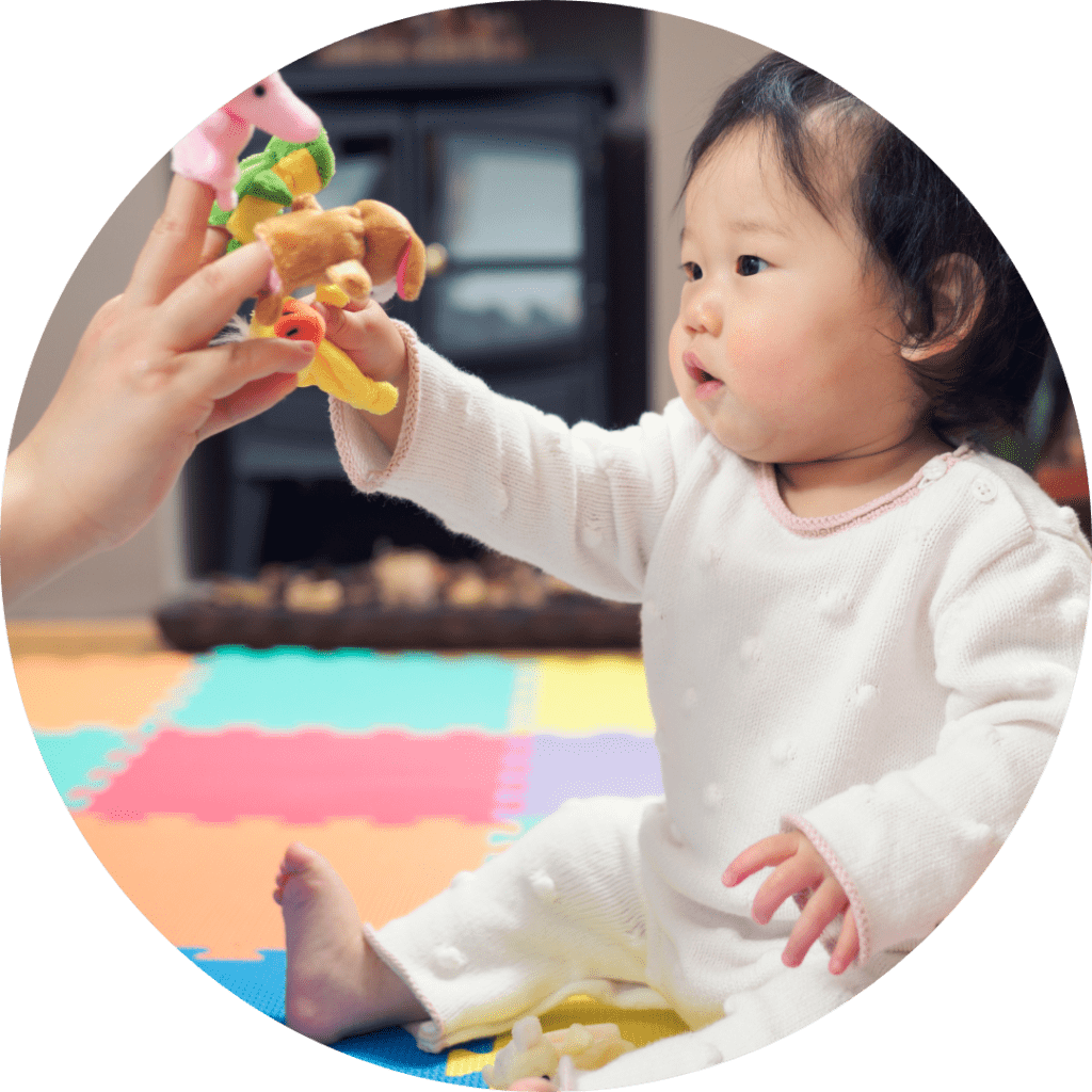 A baby reaches for finger puppets on an adult's hand.