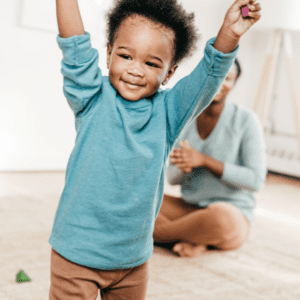 A toddler raises his arms over his head with a smile.