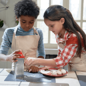 A young boy and girl grating cheese over a cutting board.