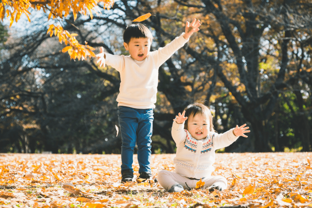 Two toddlers play outside among fall leaves.