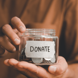 Close up of hands holding a small jar filled with coins. A label reads "donate."