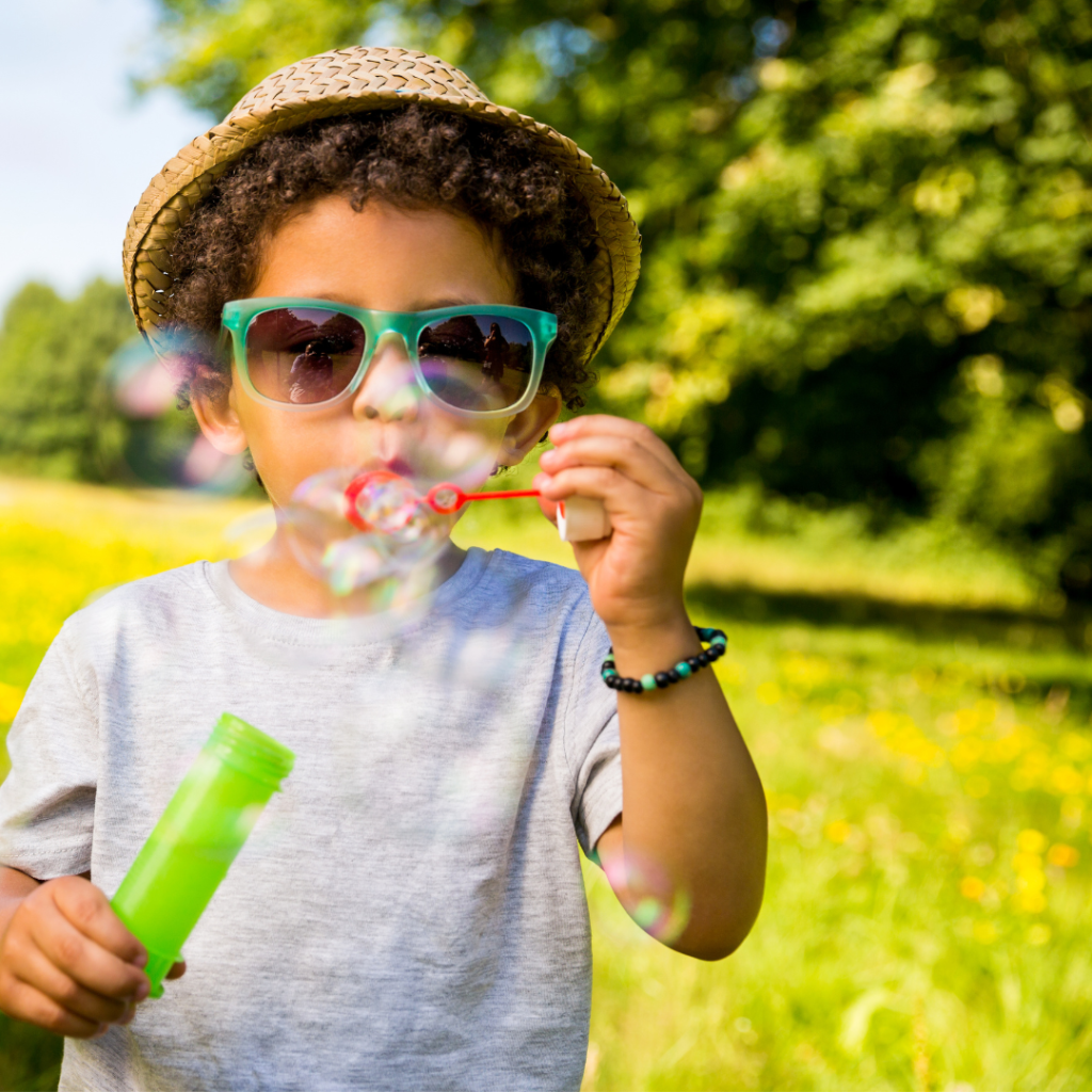 A child wearing sunglasses blows bubbles.