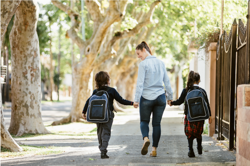 A mother holds hands with her two children as they walk to school.