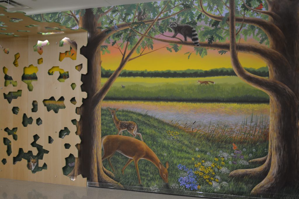 Mural of deer by a pond with wildflowers, a racoon and birds in a tree, and a fox peeking through the canopy.