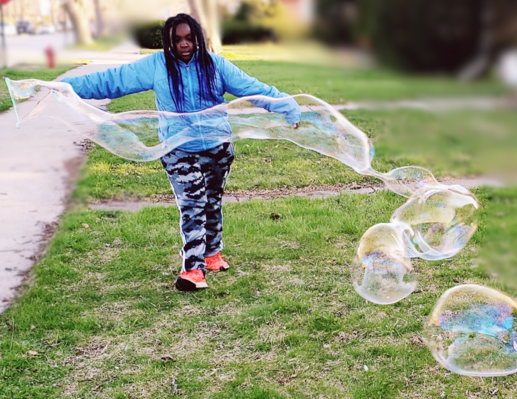 Child using giant bubble blower in the yard.